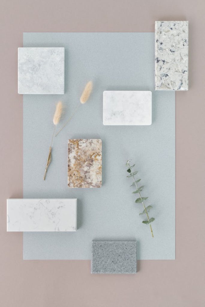 Flat lay of stone tiles and foliage on pastel background for interior design inspiration.