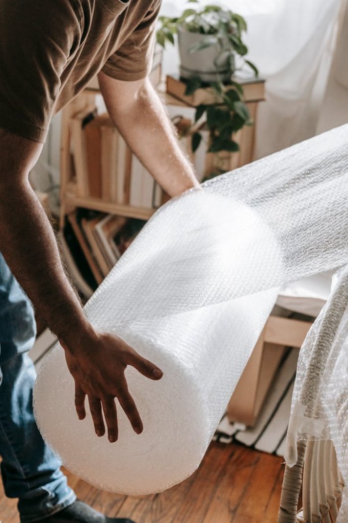 Man wrapping furniture with protective bubble wrap in a cozy indoor setting.
